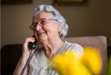 Elderly woman smiling as she holds her landline phone to her ear