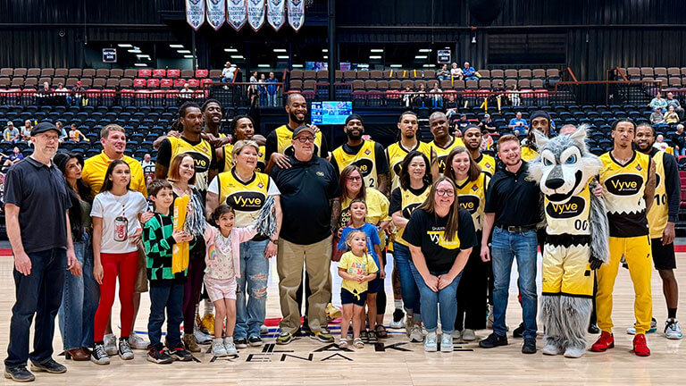 Members of the Potawatomi Fire basketball team dressed in their Vyve Broadband uniforms pose for a photo with Vyve employees and their families on the court.